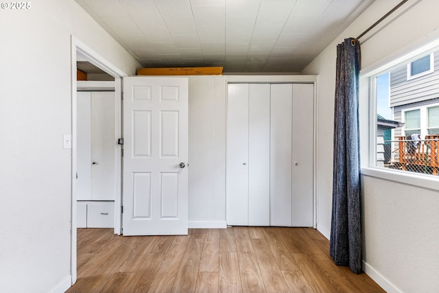 unfurnished bedroom featuring baseboards, light wood finished floors, and a closet