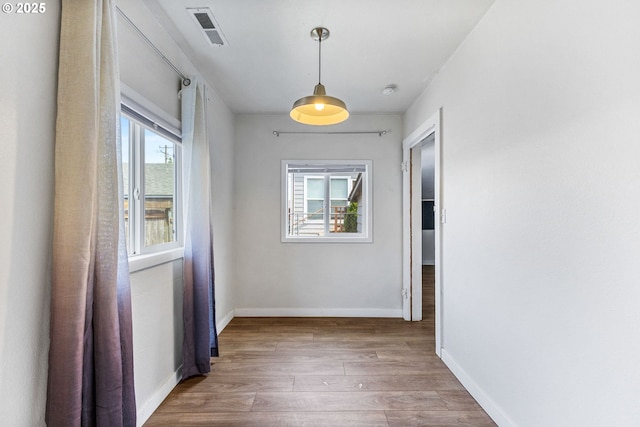 hallway featuring baseboards, a wealth of natural light, wood finished floors, and visible vents