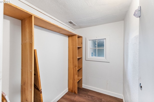 interior space featuring visible vents, a textured ceiling, baseboards, and wood finished floors