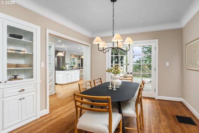 dining area featuring light wood finished floors, visible vents, crown molding, baseboards, and a chandelier