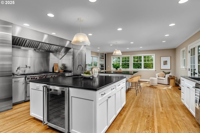 kitchen with wine cooler, a sink, dark countertops, and a kitchen island with sink