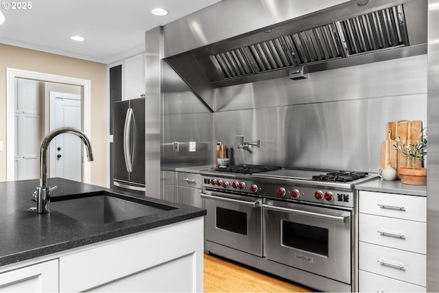 kitchen with a sink, white cabinets, appliances with stainless steel finishes, exhaust hood, and backsplash