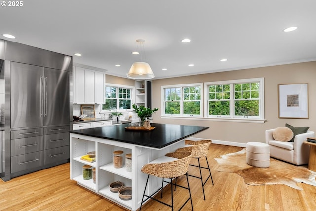 kitchen with a breakfast bar area, open shelves, white cabinetry, dark countertops, and light wood-type flooring