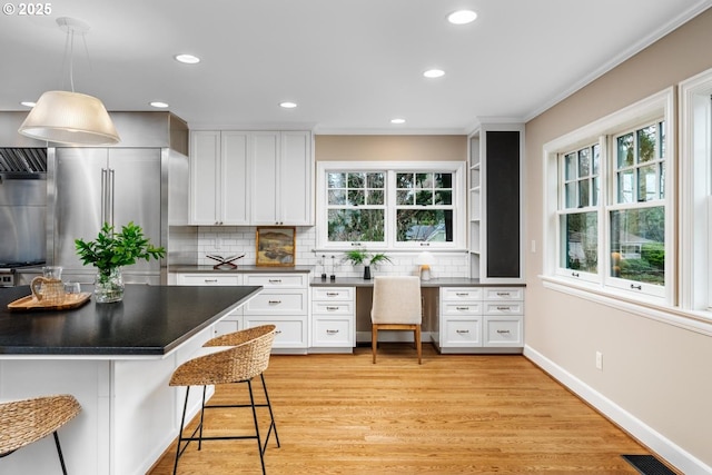 kitchen with built in study area, high end fridge, white cabinetry, dark countertops, and a kitchen breakfast bar