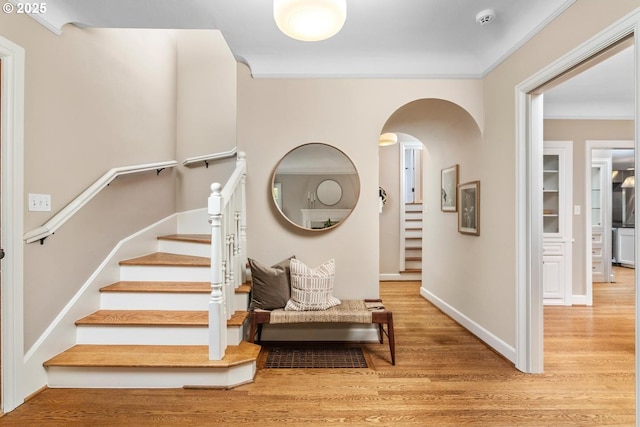 staircase featuring arched walkways, wood finished floors, baseboards, and ornamental molding