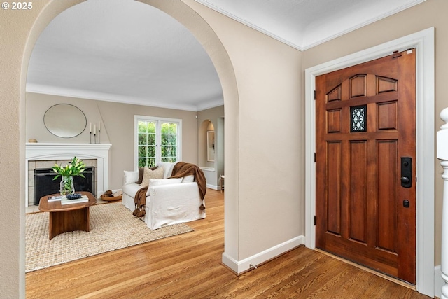 foyer entrance with baseboards, arched walkways, wood finished floors, and crown molding