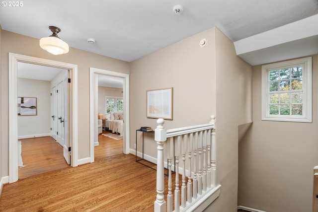 corridor with an upstairs landing, light wood-style flooring, and baseboards