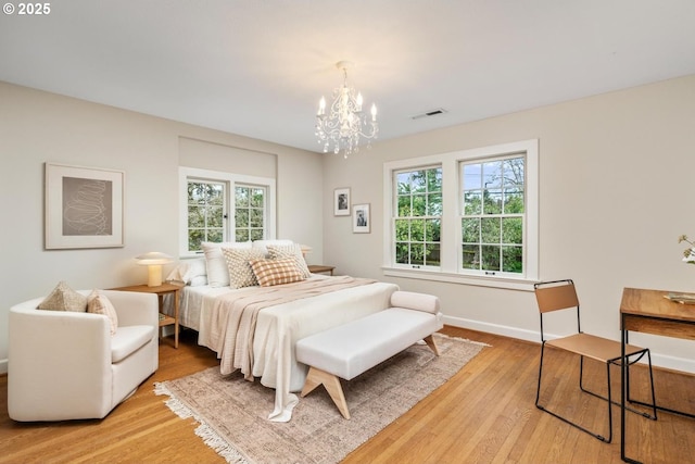 bedroom featuring light wood finished floors, visible vents, baseboards, and an inviting chandelier