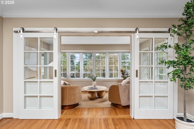 living area with ornamental molding, baseboards, a barn door, and wood finished floors