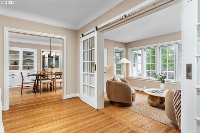 sitting room with a barn door, baseboards, a notable chandelier, and light wood finished floors