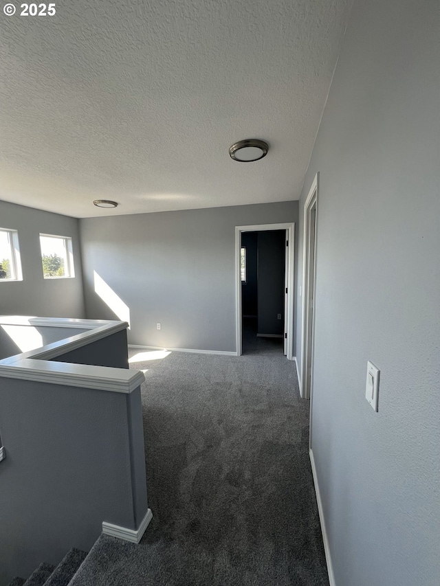 hall with a textured ceiling and dark colored carpet