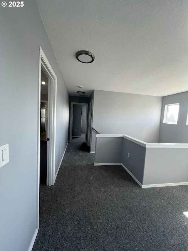 hallway featuring dark colored carpet and a textured ceiling