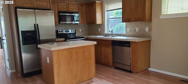 kitchen featuring sink, light hardwood / wood-style flooring, stainless steel appliances, a kitchen island, and tile countertops