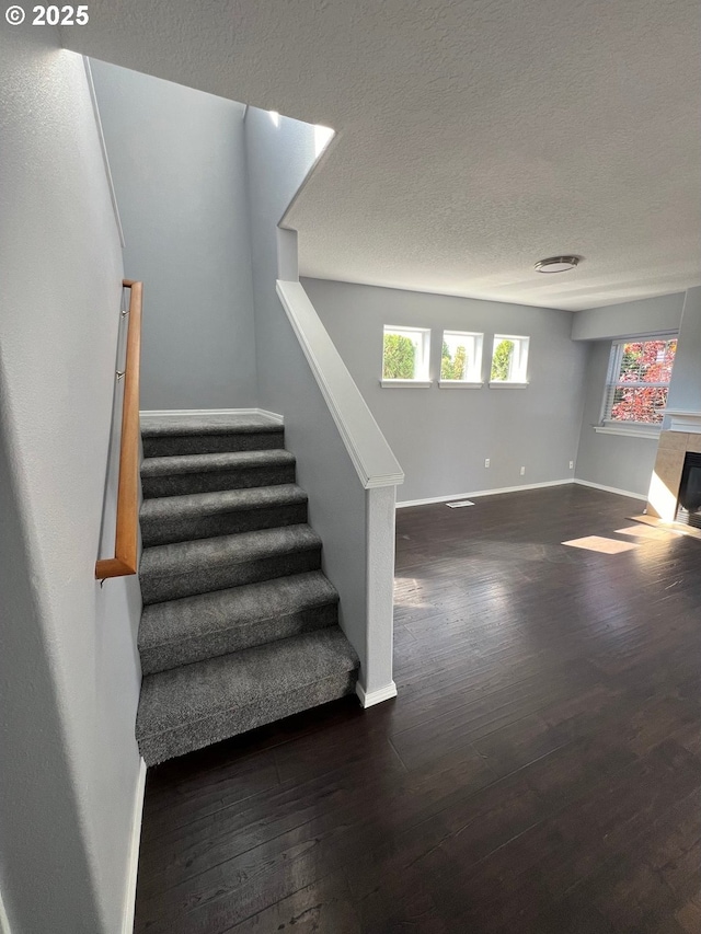 stairway with a fireplace, wood-type flooring, and a textured ceiling