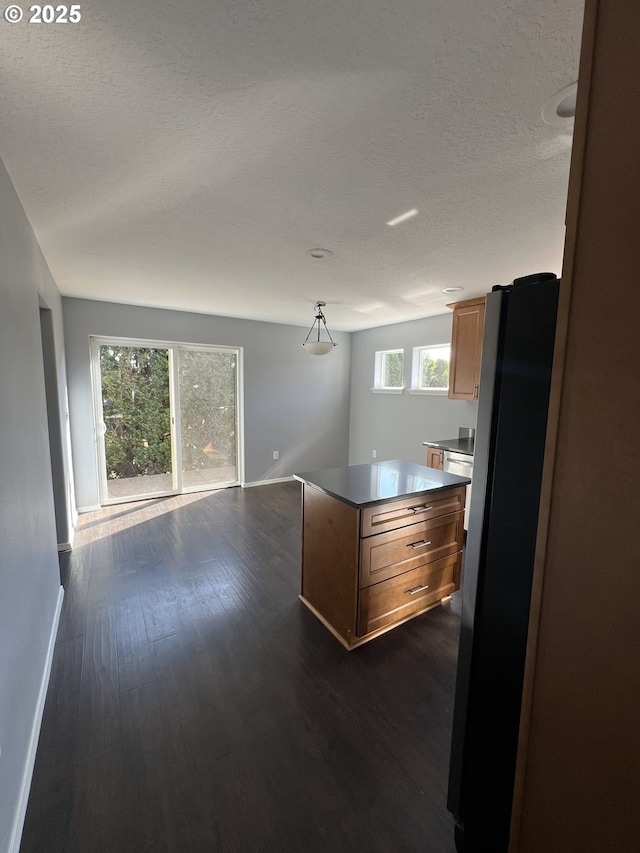 kitchen with dark hardwood / wood-style floors, decorative light fixtures, stainless steel fridge, a center island, and a textured ceiling