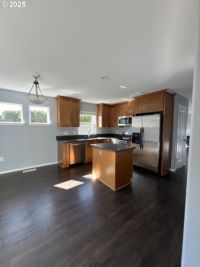 kitchen with hanging light fixtures, a textured ceiling, dark hardwood / wood-style floors, a kitchen island, and stainless steel appliances