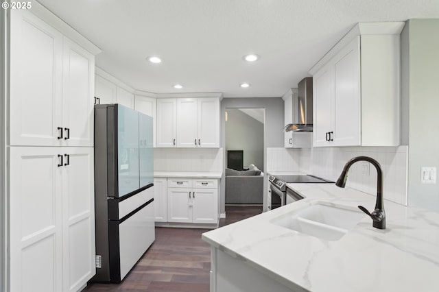 kitchen featuring a sink, stainless steel electric stove, white cabinetry, freestanding refrigerator, and wall chimney exhaust hood