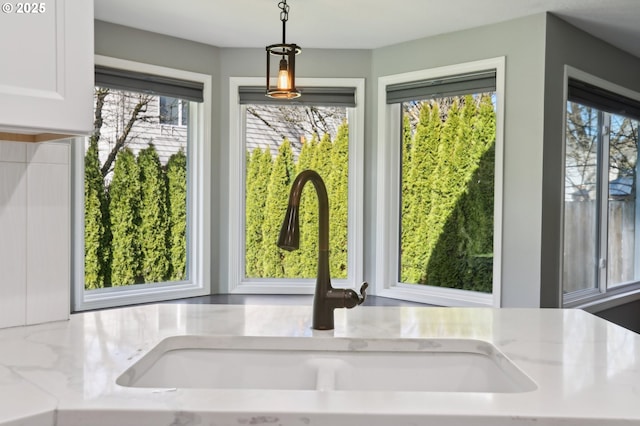 room details featuring a sink, light stone countertops, white cabinetry, and hanging light fixtures