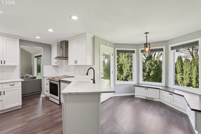 kitchen featuring electric range, backsplash, a peninsula, and wall chimney exhaust hood