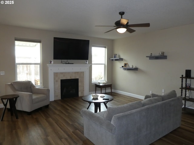 living room featuring dark wood-type flooring, ceiling fan, and a tiled fireplace