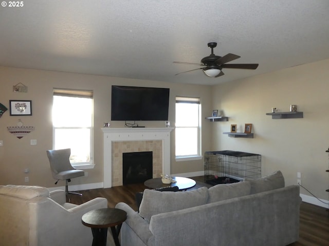 living room featuring ceiling fan, a fireplace, dark hardwood / wood-style flooring, and a textured ceiling