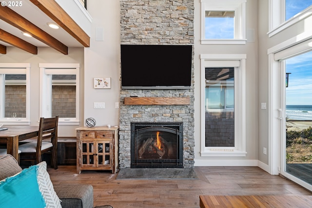 living area featuring beamed ceiling, a stone fireplace, baseboards, and wood finished floors