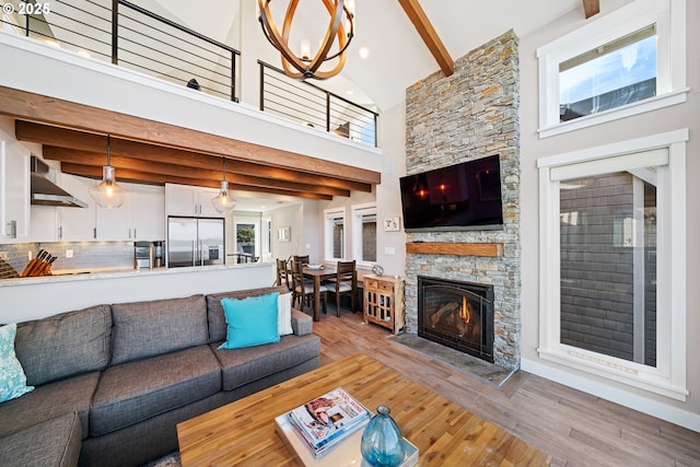 living area featuring light wood-type flooring, a notable chandelier, beamed ceiling, and a stone fireplace