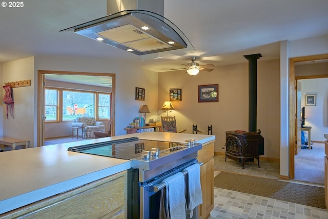 kitchen with light countertops, a ceiling fan, a wood stove, and stainless steel range with electric stovetop