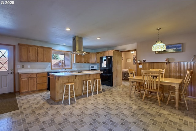 kitchen with a breakfast bar area, a kitchen island, island exhaust hood, light countertops, and freestanding refrigerator
