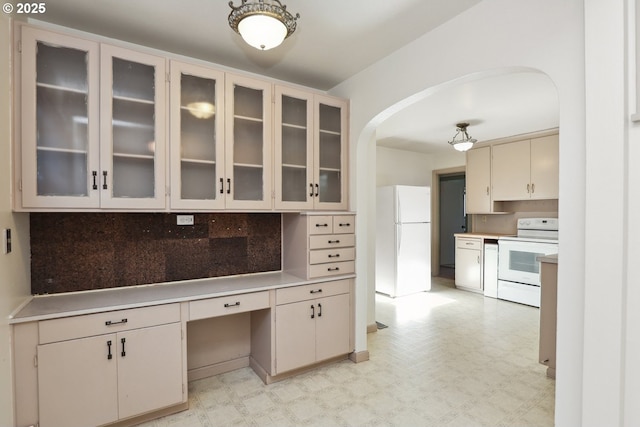 kitchen featuring white appliances, arched walkways, tasteful backsplash, and light countertops
