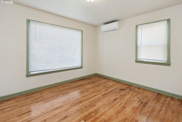 spare room with a wall unit AC, light wood-type flooring, and baseboards