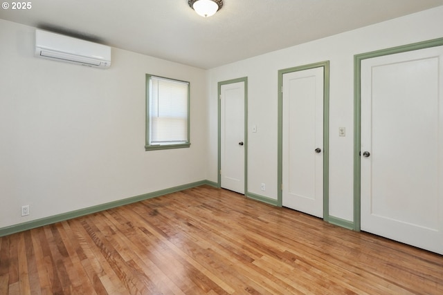 unfurnished bedroom with a wall unit AC, light wood finished floors, baseboards, and two closets