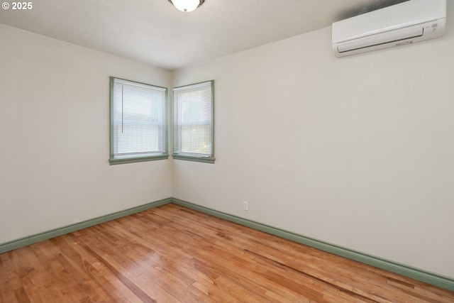 empty room featuring an AC wall unit, light wood-style floors, and baseboards