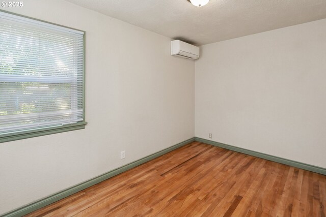 spare room featuring an AC wall unit, light wood-style flooring, and baseboards