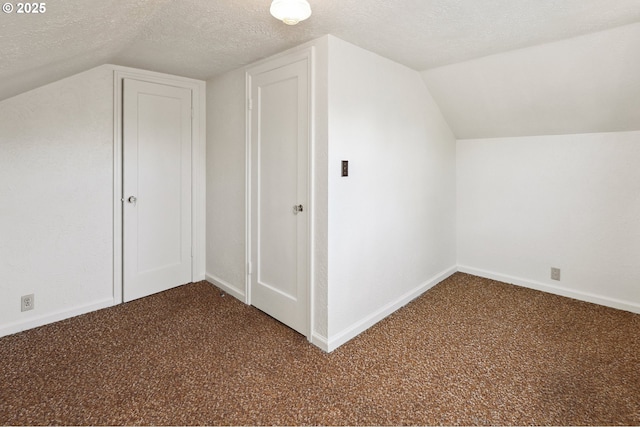 additional living space featuring dark carpet, vaulted ceiling, a textured ceiling, and baseboards