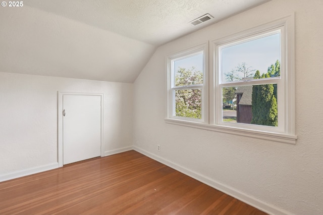 additional living space with wood finished floors, baseboards, vaulted ceiling, a textured ceiling, and a textured wall