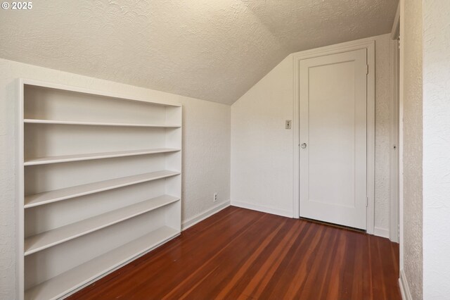 additional living space with a textured ceiling, wood finished floors, baseboards, lofted ceiling, and a textured wall