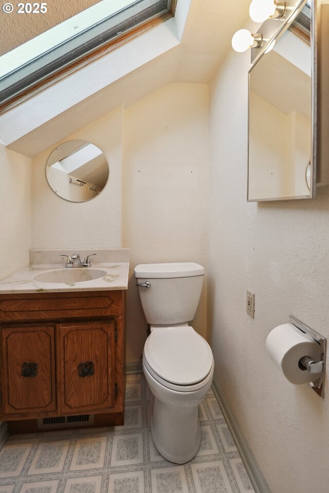half bathroom with a skylight, toilet, baseboards, and vanity
