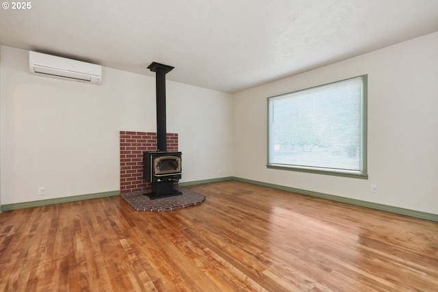 unfurnished living room featuring a wall unit AC, wood finished floors, baseboards, and a wood stove