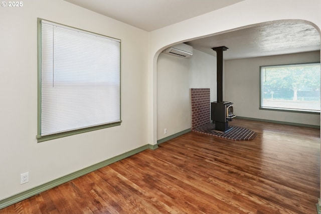 spare room with arched walkways, wood finished floors, a wood stove, and an AC wall unit