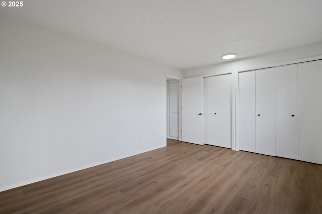 unfurnished bedroom with wood finished floors, baseboards, two closets, and a textured ceiling