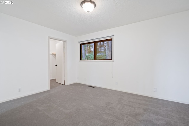 empty room with carpet flooring, visible vents, a textured ceiling, and baseboards