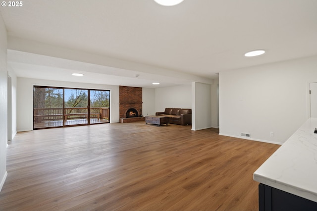 living area with a brick fireplace, baseboards, visible vents, and light wood finished floors