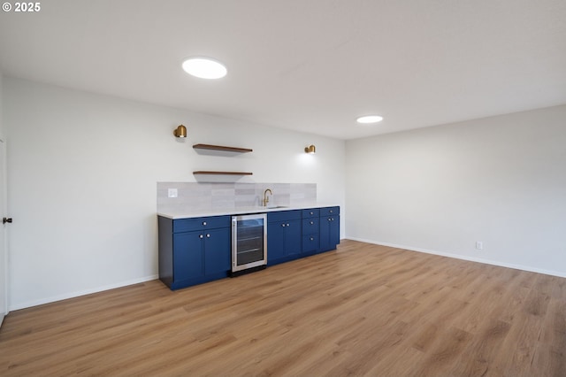 bar featuring beverage cooler, decorative backsplash, light wood finished floors, indoor wet bar, and baseboards