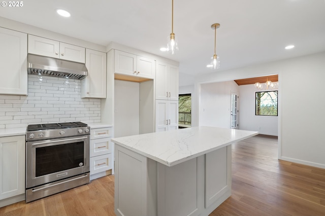 kitchen featuring light wood-type flooring, under cabinet range hood, pendant lighting, stainless steel gas stove, and backsplash