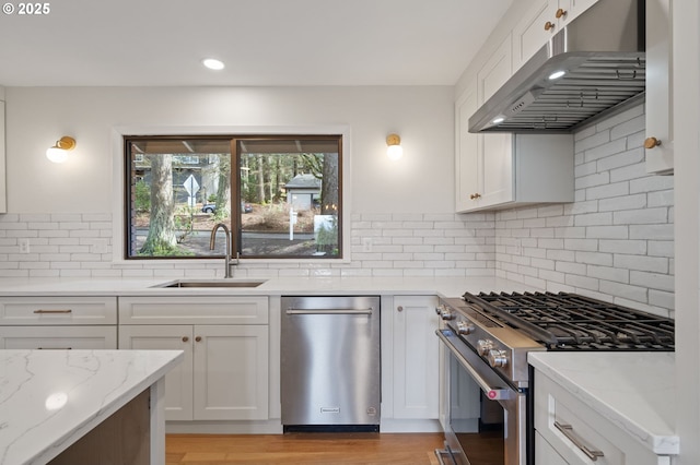 kitchen with light stone countertops, a sink, white cabinets, appliances with stainless steel finishes, and under cabinet range hood