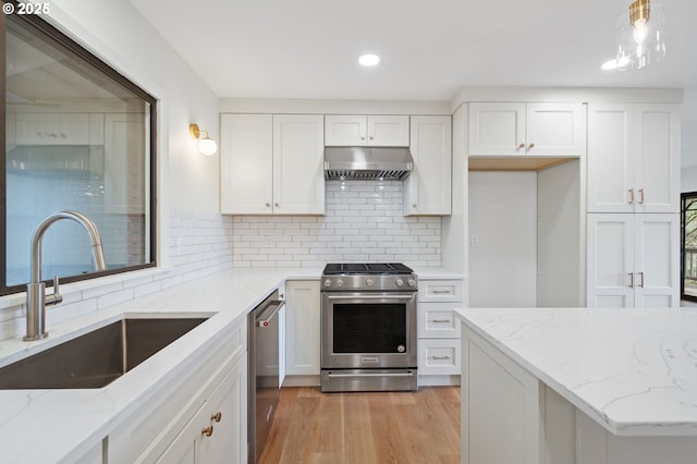 kitchen featuring light wood finished floors, under cabinet range hood, appliances with stainless steel finishes, white cabinets, and a sink