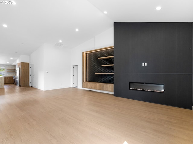 unfurnished living room with light wood-type flooring, vaulted ceiling, a fireplace, and recessed lighting