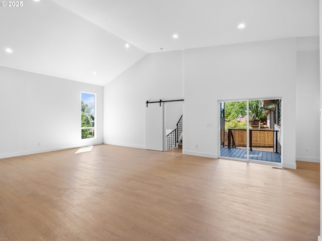 unfurnished living room with recessed lighting, a barn door, a healthy amount of sunlight, and high vaulted ceiling