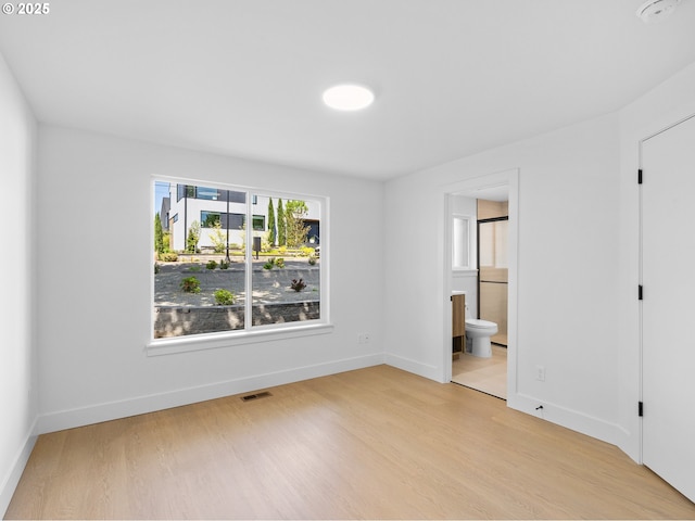 unfurnished bedroom featuring light wood-style flooring, connected bathroom, baseboards, and visible vents